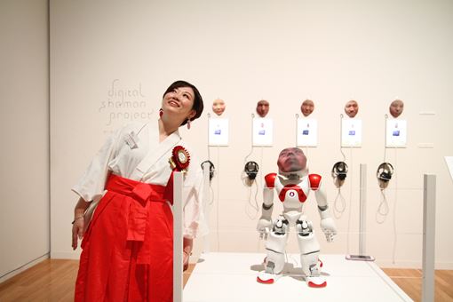 『デジタルシャーマン・プロジェクト』のロボットと同じポーズをとる市原えつこ